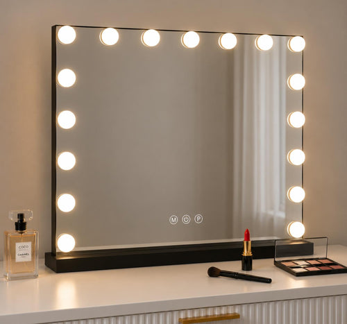 A rectangular vanity mirror with a black frame and glowing round light bulbs around the border, placed on a white dresser with cosmetics nearby.